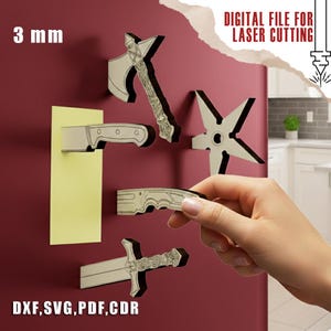 May include: A collection of laser-cut weapon-shaped magnets, including an axe, knife, shuriken, and sword, displayed on a red surface. The magnets are 3 mm thick and have a detailed design. The image also includes the text "DIGITAL FILE FOR LASER CUTTING".