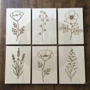 Puede incluir: Seis placas de madera con ilustraciones bot&aacute;nicas grabadas. Cada placa presenta un dise&ntilde;o floral diferente, incluyendo una amapola, delicados tallos, una rosa, lavanda, otra amapola y flores en forma de campana. Los dise&ntilde;os son de color marr&oacute;n oscuro.