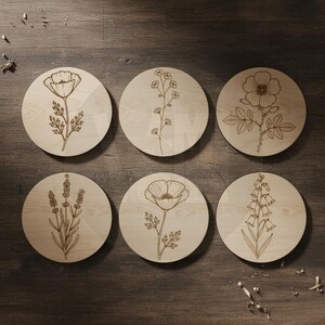 Puede incluir: Seis posavasos redondos de madera con dise&ntilde;os florales grabados. Cada posavasos presenta una ilustraci&oacute;n bot&aacute;nica diferente, incluyendo una amapola, lavanda y otras flores. Los posavasos son de madera clara y est&aacute;n dispuestos sobre una superficie de madera oscura.