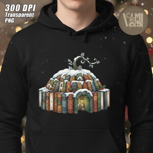 Op de afbeelding: Zwarte hoodie met een fantasie-illustratie van een huis gemaakt van boeken, bedekt met sneeuw en een tak. Het ontwerp bevat de tekst "300 DPI Transparent PNG" in de linkerbovenhoek. Een logo staat in de rechterbovenhoek.