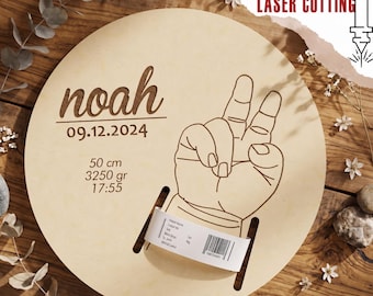 May include: A circular light-colored wooden plaque featuring the engraved name noah, the date 09.12.2024, birth statistics 50 cm, 3250 gr, 17:55, and a line drawing of a hand making a peace sign, with a hospital identification band attached.