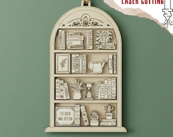 May include: Laser-cut wooden bookshelf ornament. The design includes miniature books, plants, and decorative elements. The text "THE BOOK WAS BETTER" is visible. Includes the text "DIGITAL FILE FOR LASER CUTTING".