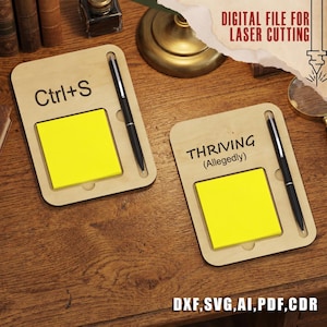 Könnte beinhalten: Zwei helle Holz-Notizhalter mit abgerundeten Ecken, jeweils mit einem quadratischen, leuchtend gelben Haftnotizzettel und einem schwarzen Stift. Ein Halter ist mit dem Text Ctrl+S und der andere mit THRIVING (Allegedly) graviert.