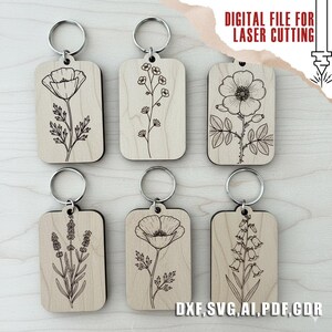 Puede incluir: Seis llaveros de madera con dise&ntilde;os florales grabados, incluyendo amapolas y lavanda. Cada llavero tiene un anillo plateado. El texto "DIGITAL FILE FOR LASER CUTTING" y abreviaturas de tipos de archivo son visibles.