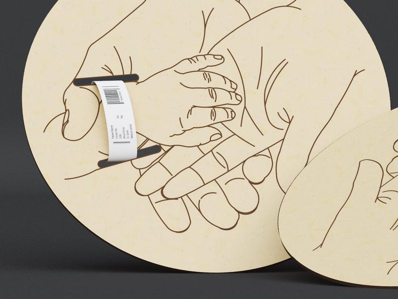 May include: Wooden family art piece featuring an outline of hands, including an adult and a child's hand, with a barcode tag. The art is on a light-colored, circular wooden base, with a second smaller piece visible.
