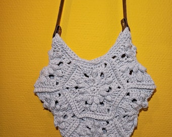 May include: A gray crocheted bag with a brown leather strap. The bag has a starburst design.