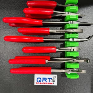 May include: A set of six red-handled pliers with green plastic holders. The pliers are organised vertically on a black surface. The holders are labelled "QRT ORGANISERS".