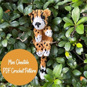 Peut inclure: Un jouet en peluche miniature de guépard crocheté avec des taches brunes et noires, des accents blancs et une longue queue. Le jouet est assis sur un lit de feuilles vertes. Le texte "Mini Cheetah PDF Crochet Pattern" est affiché sur un fond jaune.