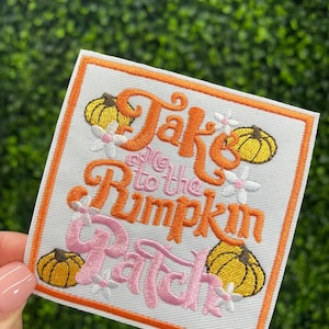 May include: Embroidered patch with the text "Take me to the Pumpkin Patch" in orange and pink. The patch features yellow pumpkins and white flowers on a white background with an orange border.