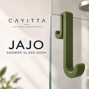 Könnte beinhalten: Ein olivgrüner Jajo Duschglashaken von Cayitta, konzipiert als doppelseitiger Haken zum Aufhängen über Glas. Der mattierte Haken besitzt ein J-förmiges Profil und ist sicher über der Kante einer transparenten Duschwand aus Glas angebracht.