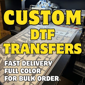 May include: A close-up of a machine printing custom DTF transfers. The text "CUSTOM DTF TRANSFERS" is printed in yellow on a white background. The text "FAST DELIVERY FULL COLOR FOR BULK ORDER" is printed in black below the main text.