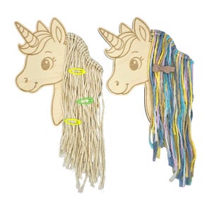 Könnte beinhalten: Zwei hölzerne Haaraccessoire-Halter in Form eines Einhornkopfes. Einer hat beigefarbenes Garnhaar mit gelben und grünen Clips. Der andere hat blaues, gelbes und rosa Garnhaar mit einer braunen Schleife. Die Einhörner haben eingravierte Details.