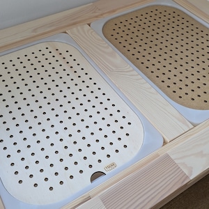 Könnte beinhalten: Zwei weiße rechteckige Tabletts mit Holzmaserung und kleinen Löchern über die gesamte Oberfläche sind in eine helle Holztischplatte eingelassen. Die Tabletts sind leicht über die Tischfläche erhöht.