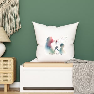 Op de afbeelding: Een wit kussen met een aquarel-silhouet van een moeder en kind die op een paardenbloem blazen. De tekst "Happy Mother's Day" staat onder de afbeelding.