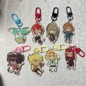 May include: A collection of anime-style character keychains. Each keychain features a unique character design with vibrant colors and attached to a metal clasp. The keychains are made of clear acrylic.