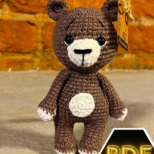 May include: A handmade brown crochet teddy bear with a white muzzle, belly patch, and paw tips. The bear has black eyes and a tag that says "Handmade". The bear is approximately 6 inches tall.
