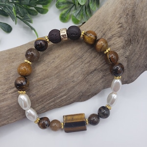May include: A brown, gold, and white beaded bracelet with a tiger's eye stone. The bracelet has a lava rock bead with a gold spacer.