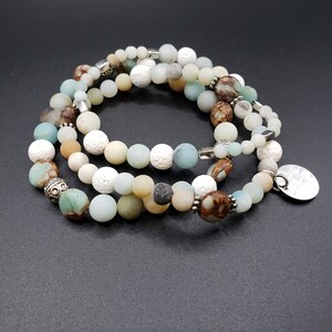 May include: A multi-strand bracelet with beads of various colors and textures, including white, brown, green, and gray. The bracelet has a silver charm with a hammered finish.