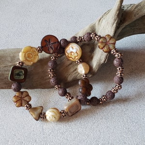 May include: Two brown beaded bracelets with various brown, white, and gold colored glass beads. The beads have different shapes and designs, including flowers, a dragonfly, and geometric shapes.