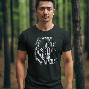 Könnte beinhalten: Ein schwarzes T-Shirt mit einem weißen Wolf-Motiv und dem Text "Verwechsle Stille nicht mit Schwäche".