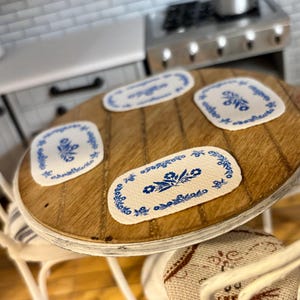 May include: A white wooden table with four white chairs. The table has a wooden top with four blue and white floral placemats.