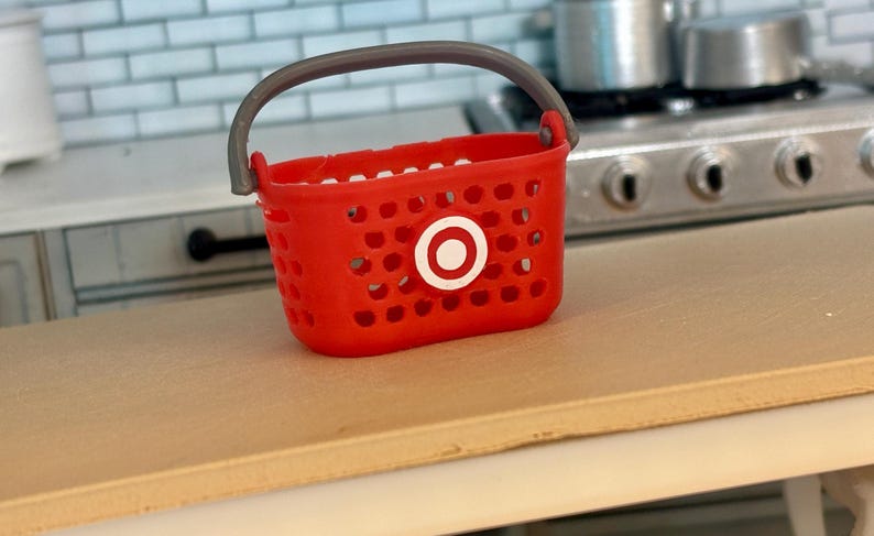 Pu&ograve; includere: Un cesto della spesa in plastica rosso con un manico grigio e un logo Target bianco.