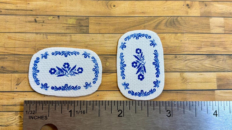 May include: Two white oval-shaped rugs with a blue floral design. The rugs are approximately 1 1/16 inches and 2 inches long.