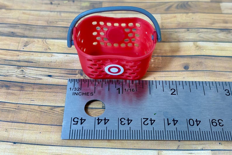Pu&ograve; includere: Un cestino della spesa in plastica rossa con un manico grigio e il logo Target. Il cestino &egrave; alto circa 2,5 cm e si trova su una superficie di legno.