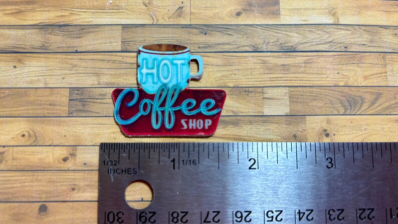 May include: A red and blue metal sign with the words "Hot Coffee Shop" and a blue coffee cup with the word "HOT" on it. The sign is about 1 1/16 inches wide.