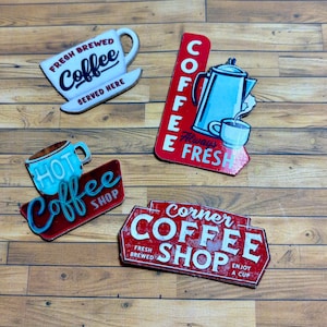 May include: Four vintage-style metal signs with red, white and blue accents advertising a coffee shop. The signs feature the words "Fresh Brewed Coffee", "Hot Coffee Shop", "Coffee Always Fresh", and "Corner Coffee Shop".
