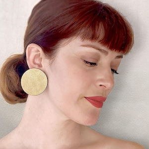 Puede incluir: Una mujer con el pelo rojo lleva unos pendientes grandes, redondos y dorados. Los pendientes son texturizados y tienen un aspecto ligeramente martillado.