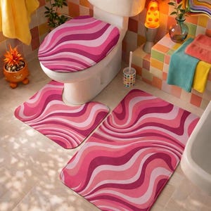 Könnte beinhalten: Ein Badezimmer-Set mit Toilettensitzbezug, U-förmigem Teppich und rechteckigem Teppich. Das Set hat ein wellenförmiges Muster in Rosa- und Weißtönen. Das Badezimmer hat einen Retro-Stil mit bunten Fliesen und einer Lavalampe.