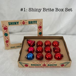 May include: A box of Shiny Brite glass Christmas tree ornaments. The box contains a dozen ornaments, including red and blue balls and a bell. The box is labeled "Shiny Brite" and "American Made".