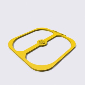 Puede incluir: Un objeto amarillo de forma cuadrada con esquinas redondeadas y un diseño central circular. El objeto tiene una extensión en forma de asa y un pequeño emblema circular en el centro. El diseño es simple y moderno, con una estética limpia.