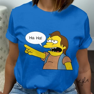 May include: Royal blue t-shirt featuring a cartoon character pointing and laughing. The character has yellow skin, brown hair, and is wearing a blue vest. A speech bubble above the character says "Ha Ha!"