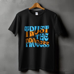 Puede incluir: Camiseta negra con el texto "TRUST THE PROCESS" en letras azules y naranjas.