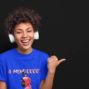 May include: A woman wearing a blue t-shirt with the text "4-MINORRRR" and a graphic of a person in a red hoodie. She is smiling and pointing to the right.