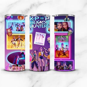 May include: Three stainless steel tumblers with a purple background featuring images and text from "K-Pop Demon Hunters". The tumblers have a wraparound design with various character illustrations and the words "GOLDEN HUNTRIX".