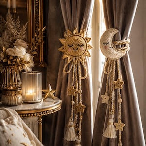 May include: Two crochet curtain tiebacks featuring a yellow sun with a smiling face and a cream-colored crescent moon with a sleeping face. Both tiebacks include long braided cords adorned with small crocheted stars, beads, and hanging tassels.