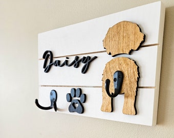 May include: White wooden dog leash rack with black hooks and a paw print. The rack has the name "Daisy" written on it in black cursive lettering.
