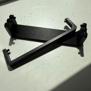 Two carbon fibre reinforced replacement battery levers, showing the hinge pins on both ends