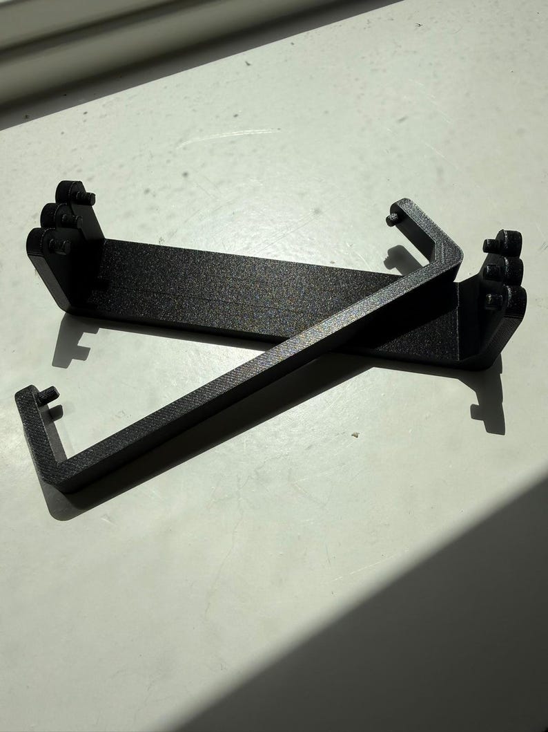 Two carbon fibre reinforced replacement battery levers, showing the hinge pins on both ends