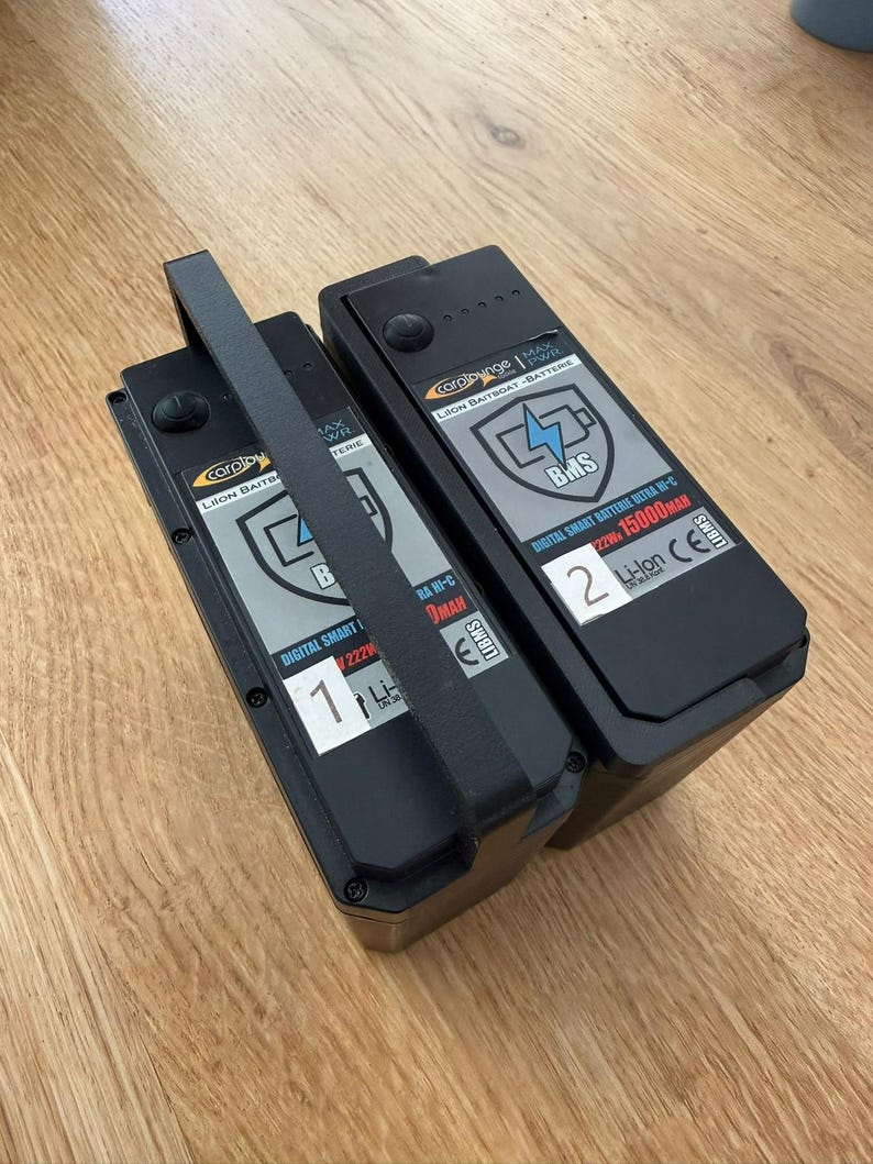 Two Carplounge smart batteries with a black 3D printed replacement lever raised as a carry handle