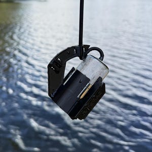 Underwater camera in the black anti-spinner hanging at an angle above the water, cable looped through the clip on the arm