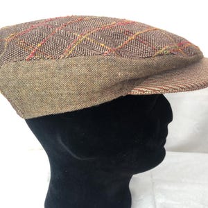Peut inclure: Une casquette plate en tweed marron avec un motif à carreaux rouge et jaune. La casquette a une visière légèrement incurvée et une sensation douce et confortable.