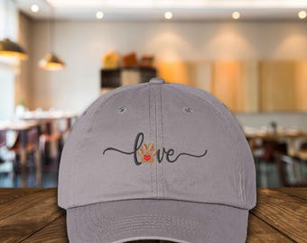 May include: Gray baseball cap with the word "love" written in cursive with a paw print and a red heart in the middle of the word.