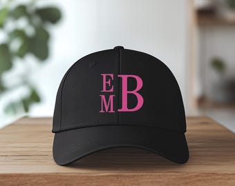 May include: Black baseball cap with pink embroidered letters "E M B" on the front.