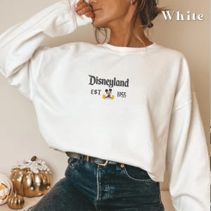 Pu&ograve; includere: Felpa bianca girocollo con la scritta "Disneyland" ricamata in nero, insieme a "EST 1955" e una grafica di Topolino. La felpa &egrave; un capo a maniche lunghe.