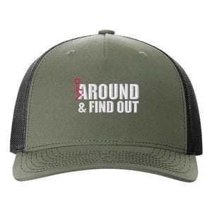 Pu&ograve; includere: Un cappello da camionista verde e nero con il testo "AROUND & FIND OUT" ricamato in bianco sul davanti. Il testo &egrave; accompagnato da un omino rosso con le braccia alzate.