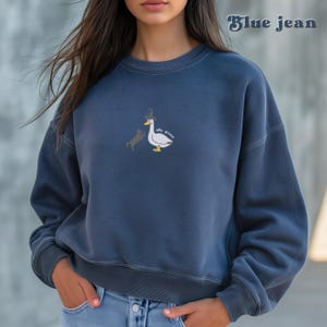 May include: A blue jean sweatshirt with a white goose and a black cat graphic on the front. The graphic says "silly goose".